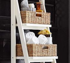 a white ladder shelf with baskets and towels on it in front of a black door