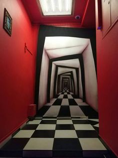 a hallway with black and white checkered flooring, red walls and framed pictures on the wall