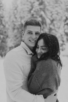 black and white photograph of a couple hugging each other in front of snow covered trees