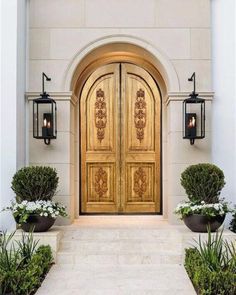 an entrance to a house with two large wooden doors and potted plants on either side