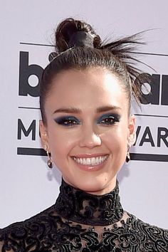 a close up of a person wearing a black dress and hair in a bun with blue eyeshadow