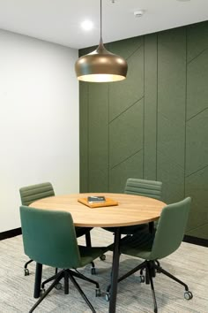 a round wooden table with four green chairs around it and a phone on top of the table