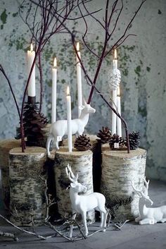 some white candles are sitting in logs with deer figurines and pine cones on them