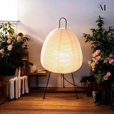 a white lamp sitting on top of a wooden floor next to potted plants and books