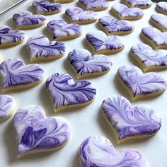 purple and white heart shaped cookies sitting on top of a cookie sheet covered in icing