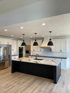 a large kitchen with an island in the middle and two lights hanging from the ceiling