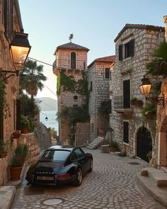 a black car parked on the side of a cobblestone road next to buildings