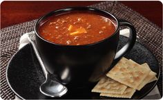 a bowl of soup and crackers on a black plate with a plaid table cloth