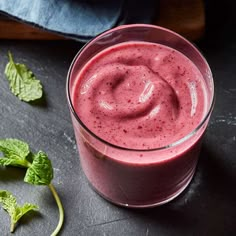 a smoothie is shown in a glass on a table with mint leaves around it