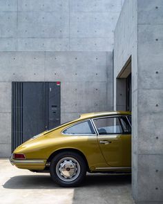 an old yellow porsche parked in front of a concrete building with its door open to the side