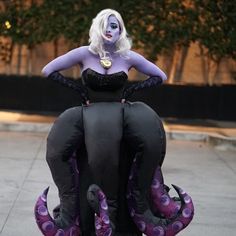 a woman in purple and black outfit sitting on top of an octopus statue with her hands behind her head