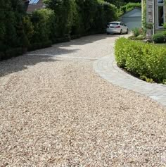 a car is parked in front of a house on a gravel driveway with trees and bushes