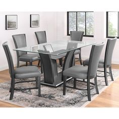 a glass dining table with grey chairs and a rug on the floor in front of it