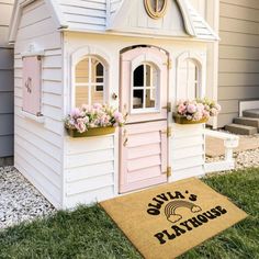 a pink and white doll house sitting on top of a grass covered lawn next to a door mat