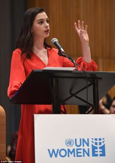 a woman standing at a podium with her hand up in the air and speaking into a microphone