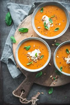 three bowls filled with carrot soup on top of a wooden cutting board