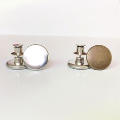 two silver cufflinks and one brown button on a white surface with light reflection