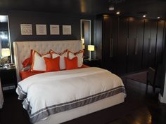 a bed with white and orange pillows on top of it next to a night stand