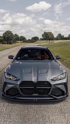 the front end of a gray sports car on a road with grass and trees in the background