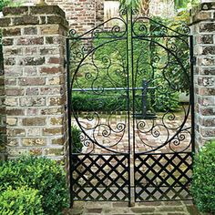 an iron gate in the middle of a brick wall with bushes and shrubs around it