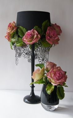 two black vases with pink roses in them on a white tablecloth next to a black lamp shade