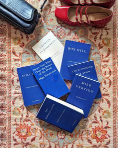 four blue books sitting on top of a rug next to red shoes and purses