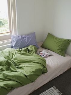 an unmade bed with green sheets and pillows on it in front of a window