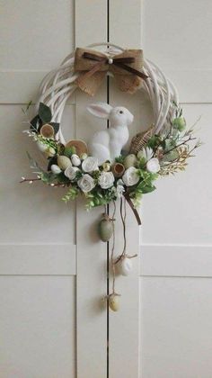 a wreath with flowers and a bunny on it hanging from the front door, decorated with greenery