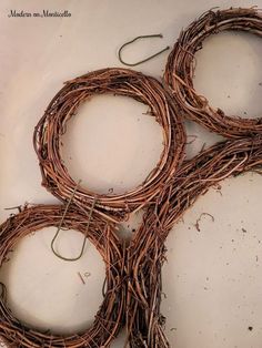 four wreaths made out of twigs sitting on top of a white surface with string attached to them