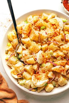 a white bowl filled with potato salad next to some seasoning