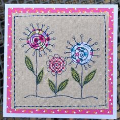 two flowers are on the side of a piece of fabric with pink and blue trim