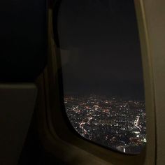 an airplane window with the view of city lights at night from it's seat