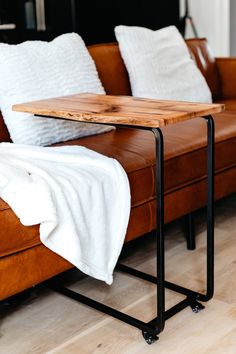 a wooden table sitting on top of a brown couch next to a white blanket and pillows