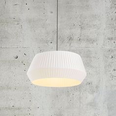 a white lamp hanging from the ceiling in front of a concrete wall with dots on it