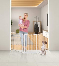 a woman holding a baby standing in front of a gate with a dog on the other side