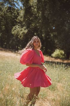 a woman in a pink dress standing in tall grass