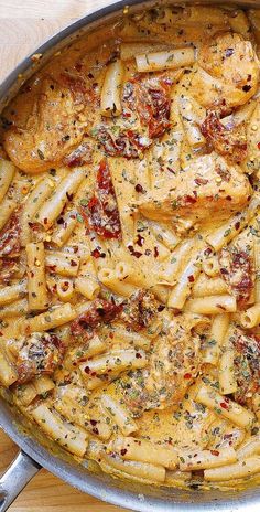 a skillet filled with pasta and sauce on top of a wooden table