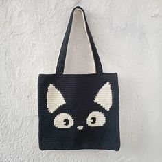 a crocheted black and white cat bag hanging on a wall with the eyes open