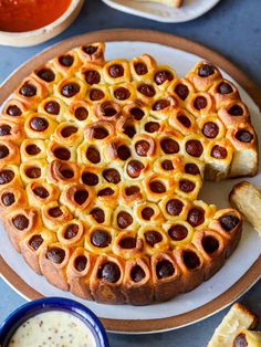 a pizza on a plate next to some bread and dipping sauces in small bowls