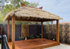 a wooden gazebo with a thatched roof and bamboo flooring in a backyard