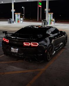 a black sports car parked in a parking lot next to a gas station at night