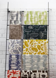 four different colored tea towels hanging on a rack against a white brick wall with black iron bars