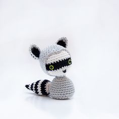 a crocheted raccoon sitting on top of a white surface with green eyes