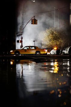 a yellow car driving down a street next to a traffic light on a rainy night