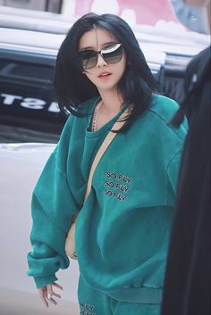 a woman with black hair wearing a green sweatshirt and matching sunglasses is walking down the street