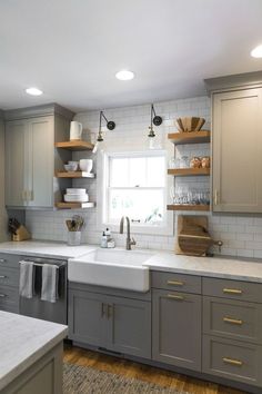 a kitchen with gray cabinets and white counter tops, open shelving above the sink