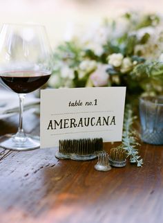 a wooden table topped with a wine glass filled with red wine next to a sign