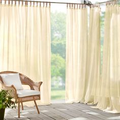 a wicker chair sitting in front of a window with white drapes on it