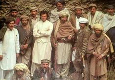 a group of men standing next to each other in front of a stone wall and grass field