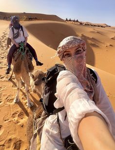 two people riding camels in the desert with their faces covered by veils and headgear